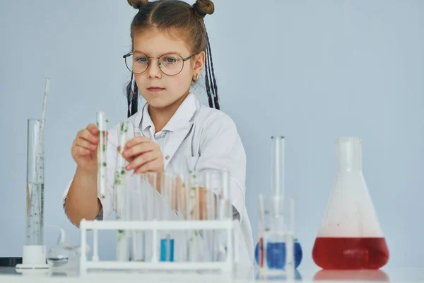 Works with test tubes. Little girl in coat playing a scientist in lab by using equipment.