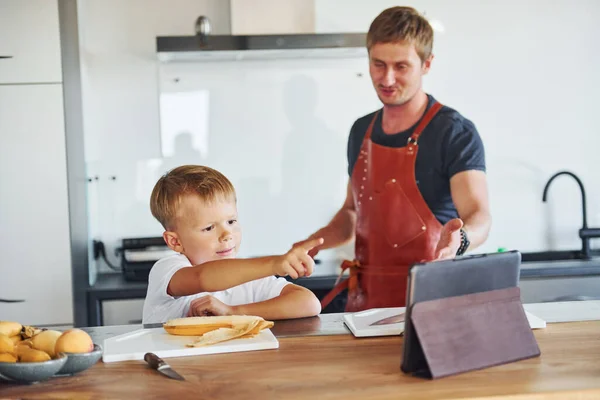 Using tablet to learn how to cook. Father and son is indoors at home together.