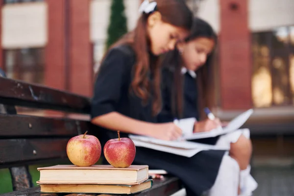Books and apples. Two schoolgirls is outside together near school building.