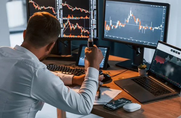 Alkolle. Resmi giyinmiş genç işadamı birden fazla ekranla ofiste..