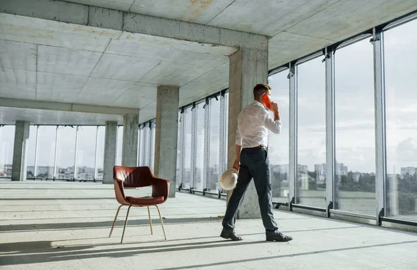 Telefon kullanarak sohbet ediyorlar. Resmi kıyafetli genç adam içeride inşaatta çalışıyor..