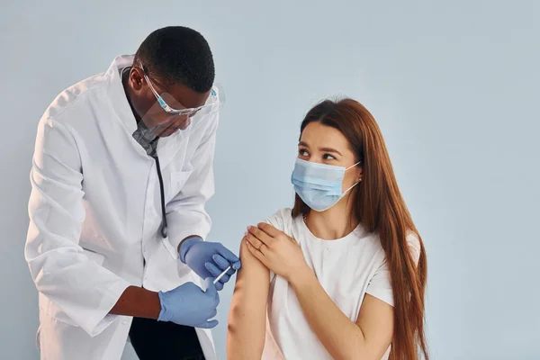 Young african american doctor giving injection to woman at hospital.