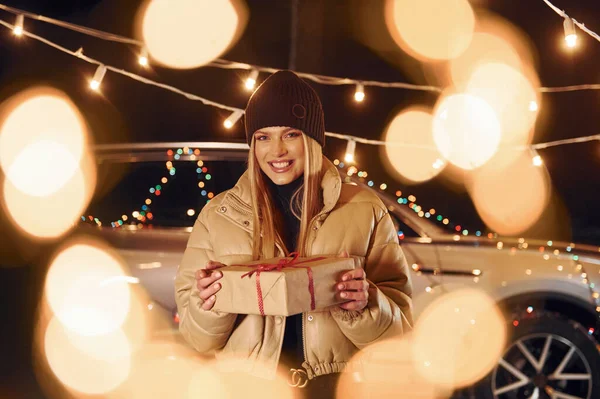 Holding gift box. Woman standing in the forest and celebrating New year.