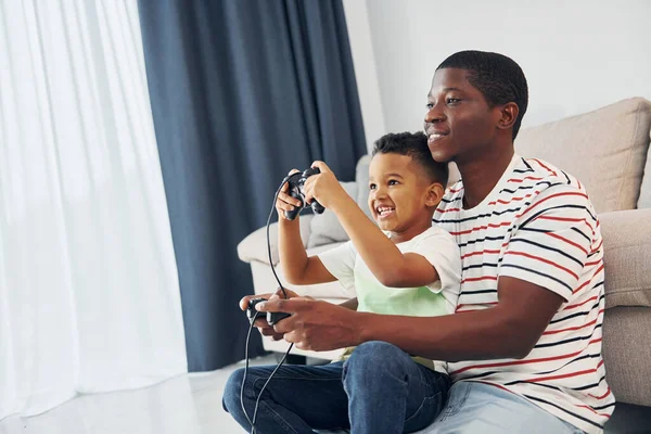 Jugando Videojuegos Padre Afroamericano Con Hijo Pequeño Casa Imagen de stock