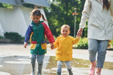 Ön manzara. Anne, küçük oğlu ve kızıyla yağmurdan sonra parkta yürüyüşe çıktı..