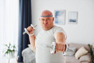 Dambıl kullanıyor. Sıradan giysili komik şişman adam evde..