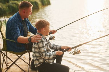 Dinleniyor ve eğleniyor. Baba ve oğul yazın birlikte açık havada balık avlıyorlar..