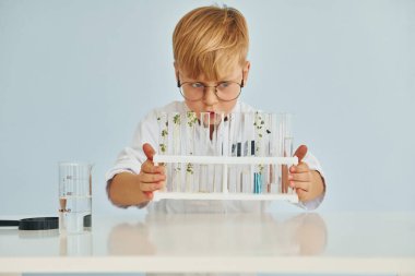 Test tüpleri kullanıyor. Palto giyen küçük çocuk laboratuarda ekipman kullanarak bilim adamı rolü oynuyor..