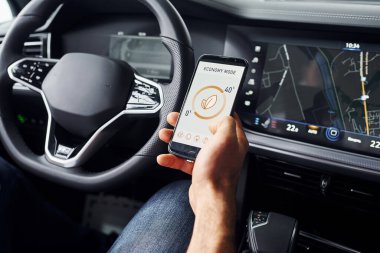 Arabada oturuyordu. Etiketli ve simgeli telefonları tutan adamın elini yakından izle. Uzaktan kumanda kavramı.