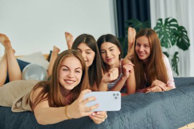 Akıllı telefonla yatağa uzanmak. Bir grup mutlu kadın bekarlığa veda partisindeler..
