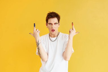 Genç eşcinsel adam stüdyoda duruyor ve kameraya poz veriyor. Gökkuşağı makyajı.