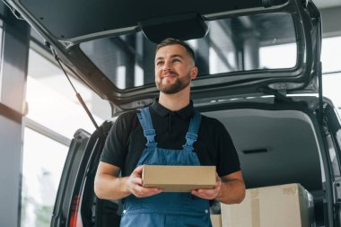 Olumlu duygular. Üniformalı teslimatçı içeride arabasıyla ve siparişiyle bekliyor..