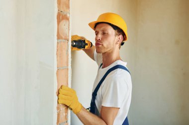 Kapalı bir odada, bitmemiş bir odada. Gündüz vakti inşaatta üniformalı genç bir adam çalışıyor..