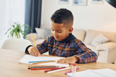 Masanın yanında oturuyor. Neşeli genç çocuk evde yalnız..