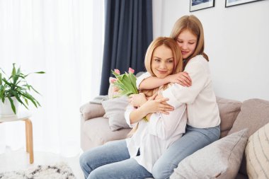 Sarılmak ve çiçek vermek. Genç anne ve kızı gündüz vakti evdeler..