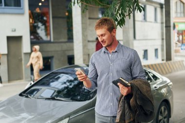 Elinde not defteriyle. Gündüz vakti şehirde gezen bir adam..