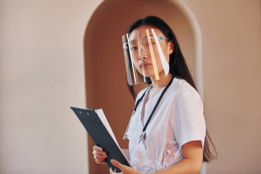 Koruyucu giysi içinde. Genç ciddi Asyalı kadın içeride duruyor..