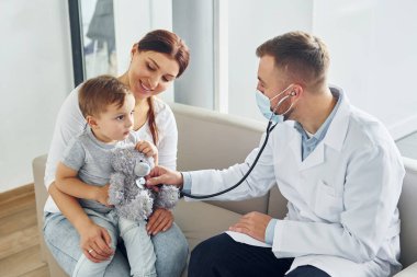 Çocuğa yardım ediyorum. Beyaz önlüklü iki doktor klinikte birlikte çalışıyorlar..