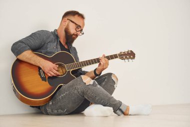 Stüdyoda. Gündelik giysiler içinde ve akustik gitarlı bir adam içeride..