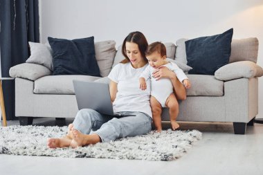 Gümüş renkli laptop. Anne ve küçük kızı evde birlikte..
