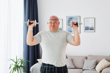 Dambıl kullanıyor. Sıradan giysili komik şişman adam evde..