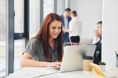 Meslektaşlarının önünde bir kadın. Ofiste resmi giysiler içinde bir grup insan var..