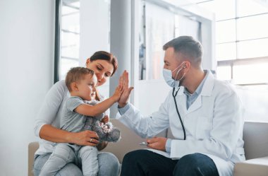 Çocuğa yardım ediyorum. Beyaz önlüklü iki doktor klinikte birlikte çalışıyorlar..
