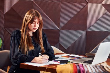 Kadın elinde laptop ve belgelerle masada oturuyor. Yeni lüks restoranın içinde..