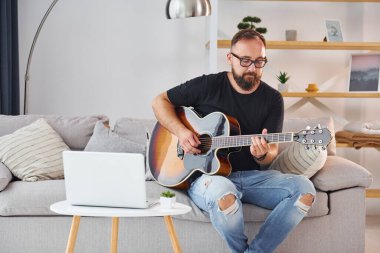 Laptop kullanıyorum. Gündelik giysiler içinde ve akustik gitarlı bir adam içeride..
