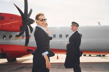 Pilot ve hostes. Havaalanı ve uçak işçileri resmi giysiler içinde dışarıda birlikte duruyorlar..
