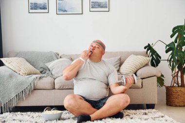 Yemek yiyor ve egzersiz yapıyor. Sıradan giysili komik şişman adam evde..