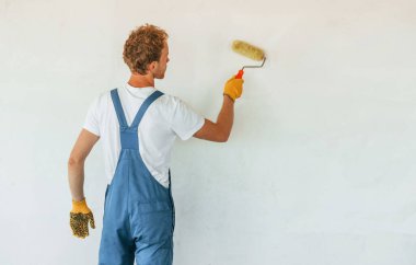 Temiz duvarlar. Gündüz vakti inşaatta üniformalı genç bir adam çalışıyor..