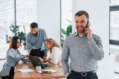 Telefonlu bir adam. Ofiste proje üzerinde çalışan bir grup iş adamı..