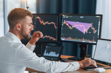 Grafikler aşağı iniyor. Resmi giyinmiş genç işadamı birden fazla ekranla ofiste..