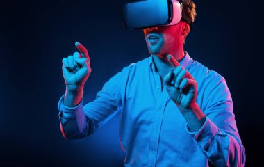 Sanal gözlüklerle. Neon ışıkları. Genç Avrupalı adam karanlık stüdyoda..