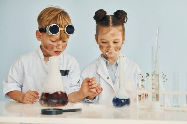 Çocuk test tüplerinde sıvı ile çalışıyor. Beyaz önlüklü çocuklar laboratuarda ekipman kullanarak bilim adamlarını oynuyorlar..