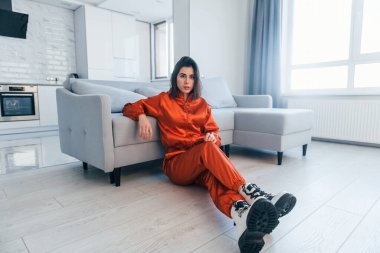 Kırmızı kostümlü bir kamera için poz vermek. Genç kadın, gündüz vakti modern evin içinde..