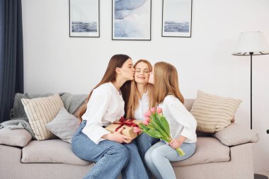 Hediyelerle oturmak. Genç anne ve iki kızı gündüz vakti evdeler..