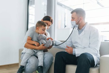 Küçük çocuk inceleniyor. Beyaz önlüklü iki doktor klinikte birlikte çalışıyorlar..