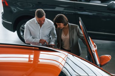 Birbirleriyle iletişim kuruyorlar. Resmi kıyafetli adam, müşteriye otomobil seçiminde yardımcı oluyor..