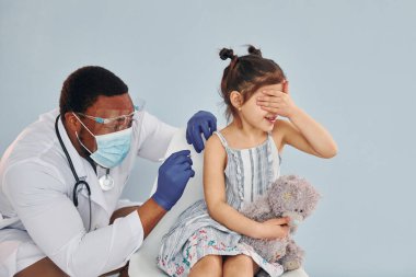 Genç Afrikalı Amerikalı doktor hastanedeki küçük kıza iğne yapıyor..