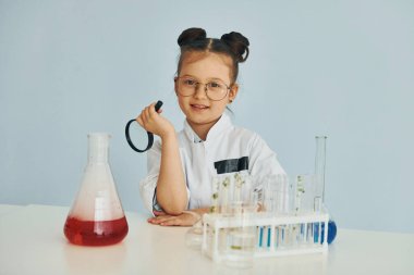 Test tüpleriyle çalışıyor. Palto giyen küçük bir kız laboratuarda ekipman kullanarak bilim adamını oynuyor..