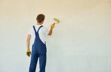 Temiz duvarlar. Gündüz vakti inşaatta üniformalı genç bir adam çalışıyor..