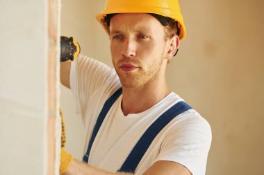 Ekipmanlarla. Gündüz vakti inşaatta üniformalı genç bir adam çalışıyor..