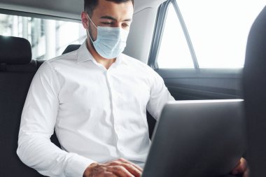 Dizüstü bilgisayarla çalışıyor. Beyaz gömlekli genç adam modern bir otomobilin içinde oturuyor..