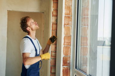 Koruyucu eldivenlerle. Gündüz vakti inşaatta üniformalı genç bir adam çalışıyor..