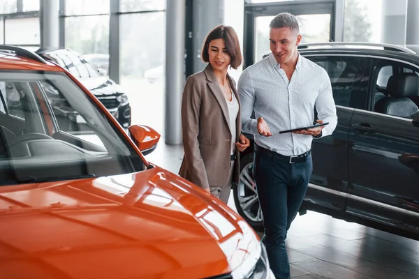 Not defteriyle. Resmi kıyafetli adam, müşteriye otomobil seçiminde yardımcı oluyor..