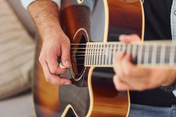 Close up view. Man in casual clothes and with acoustic guitar is indoors.