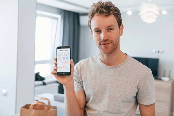 Young man in casual clothes is indoors controlling smart home technology.