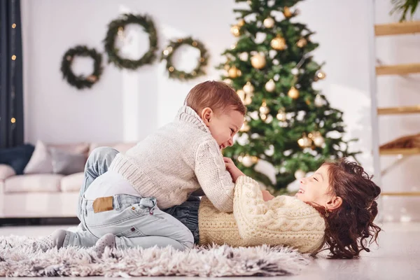 Uzanmak ve oynamak. Küçük kız ve erkek kardeş noel süsleme odasında beraberler..